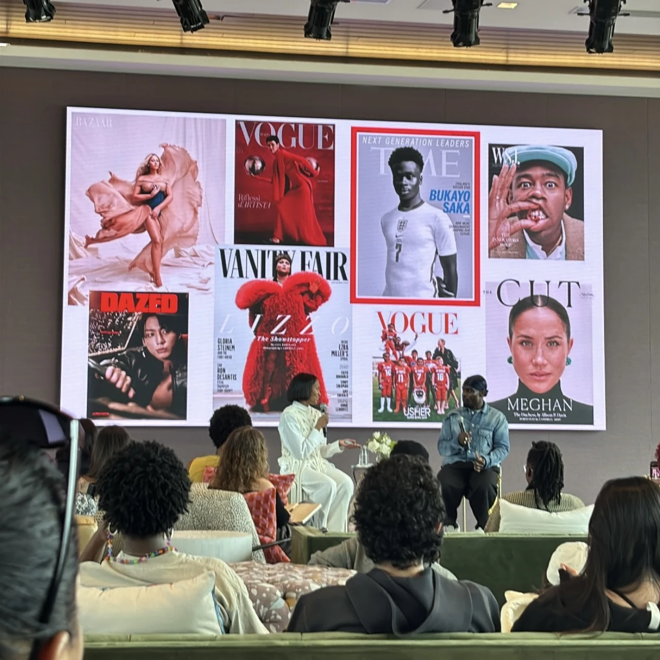 Alex Delotch Davis speaking on stage with magazine covers displayed behind her